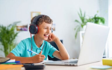 Ein Junge mit Kopfhörern sitzt an einem Schreibtisch, konzentriert auf seinen Laptop, vertieft in seine Arbeit oder Unterhaltung.