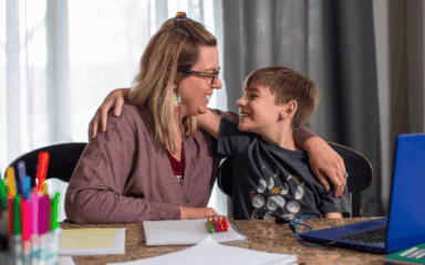 Eine Frau und ein Junge sitzen an einem Tisch und beschäftigen sich mit einem Laptop, der vor ihnen steht.