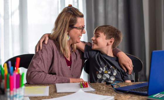 Eine Frau und ein Junge sitzen an einem Tisch und beschäftigen sich mit einem Laptop, der vor ihnen steht.